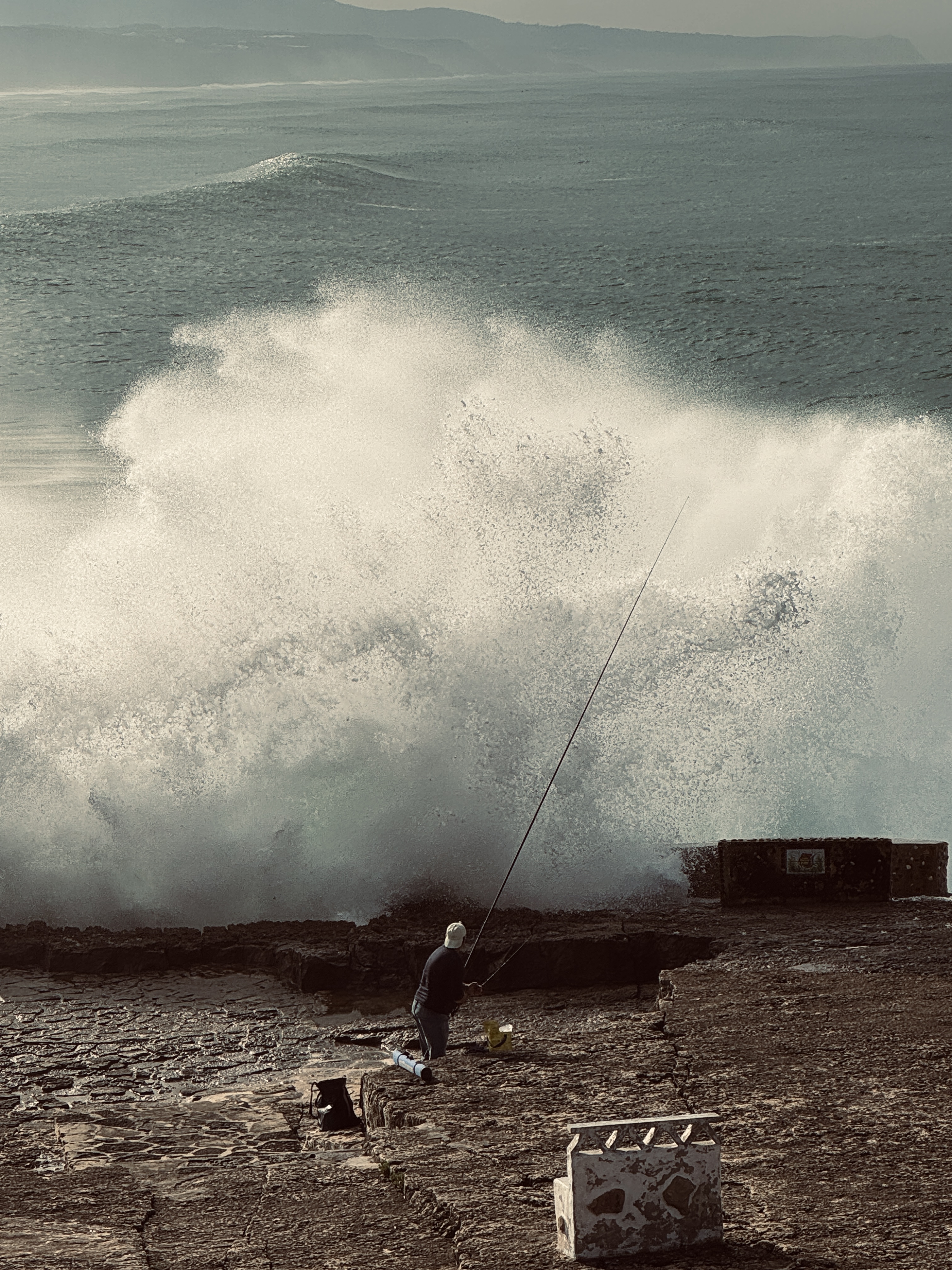Fisherman casting a line from the rocks as large Atlantic waves crash behind him