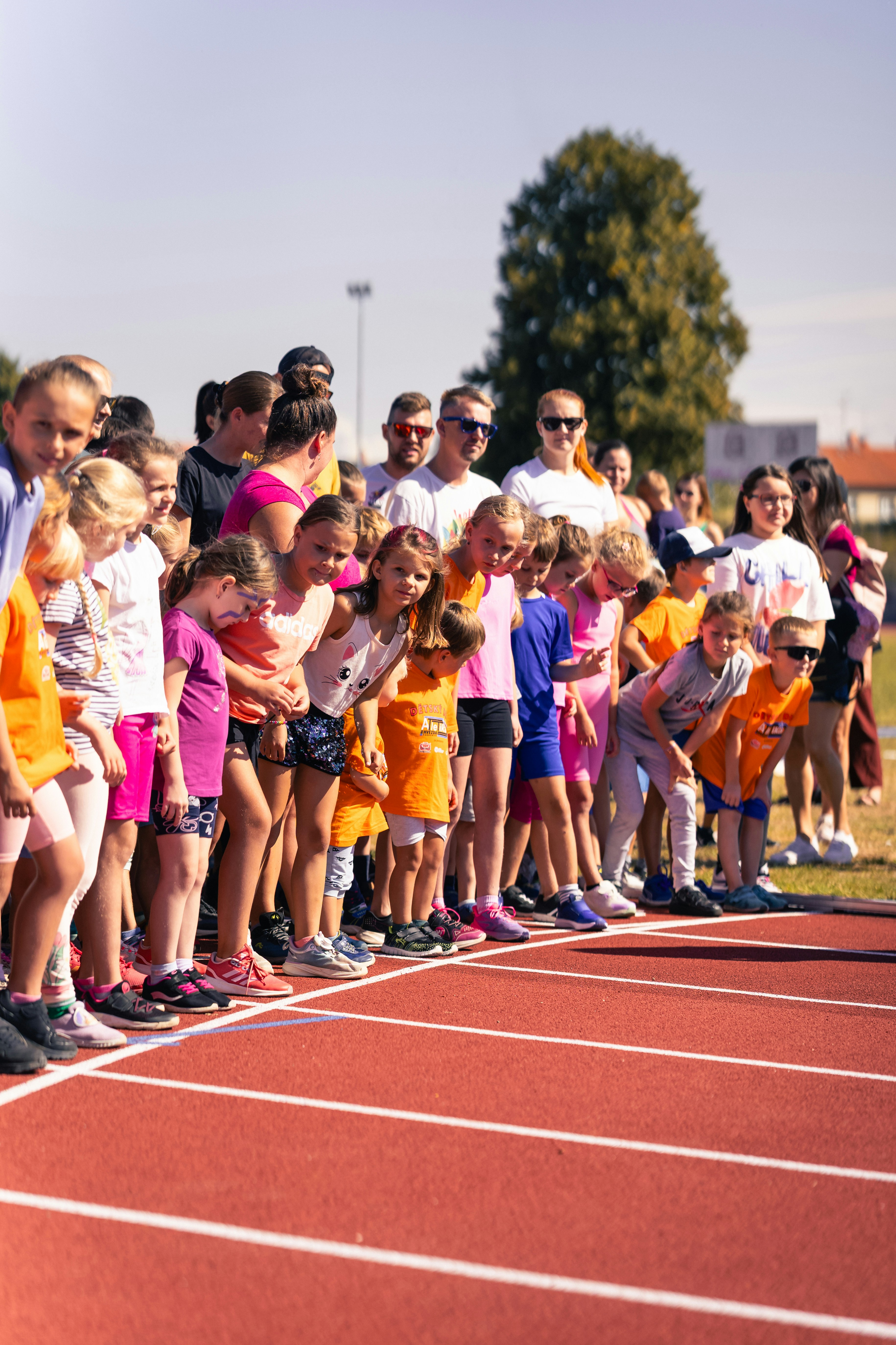 Children and adults lined up at the start of a running track on a sunny day