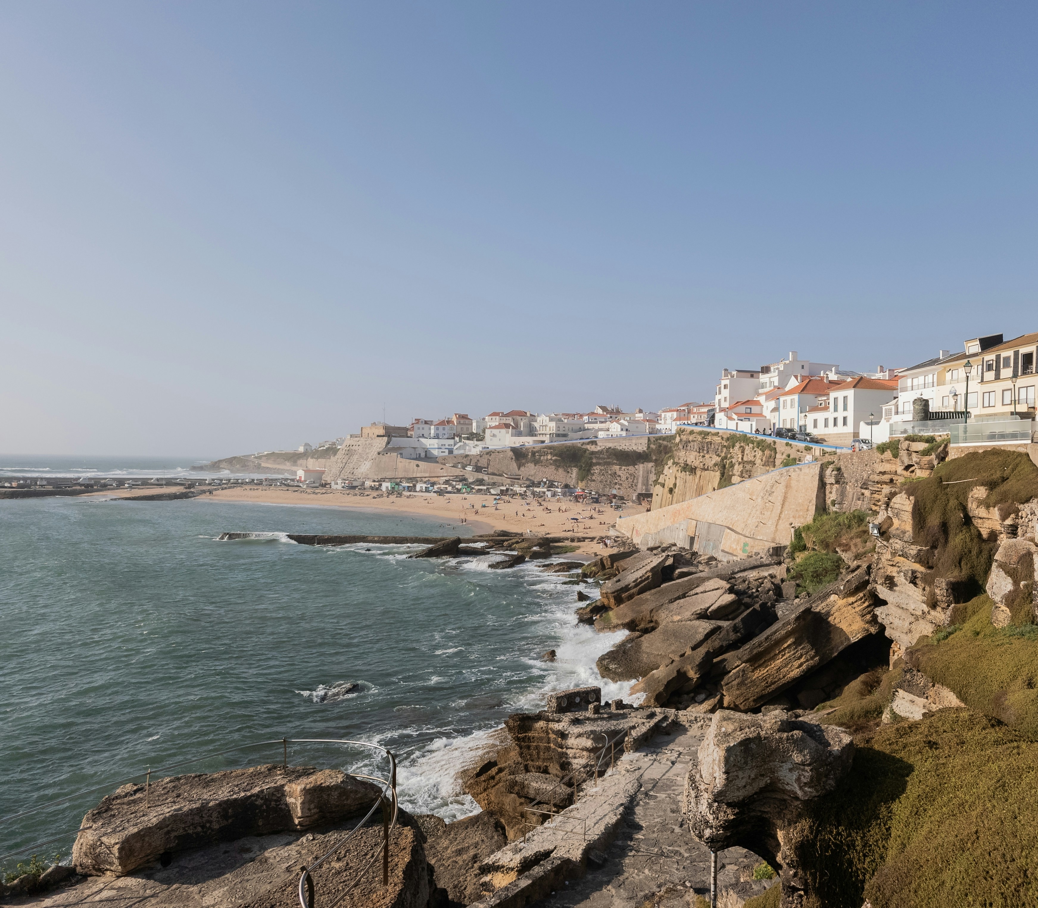 Ericeira's rocky coastline with a sandy beach and whitewashed town perched on the cliffs above the Atlantic